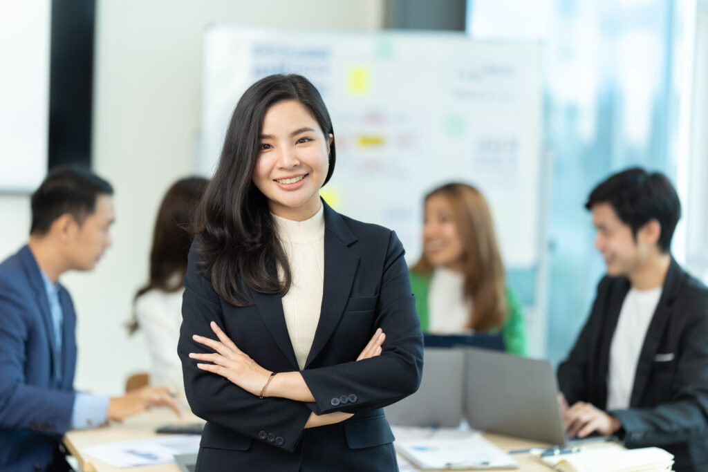A corporate intern standing confidently with her colleagues discussing behind her.